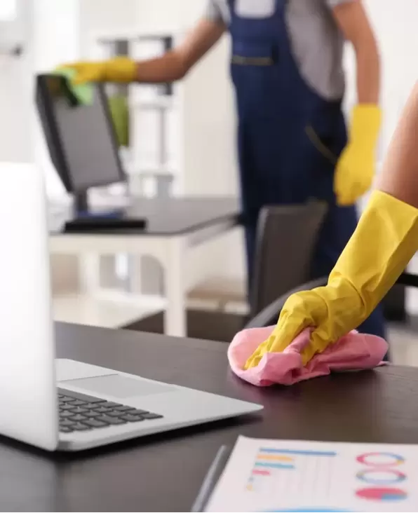 Cleaning professionals in an office dusting desks and monitors